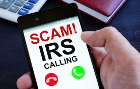 A cell phone that shows an IRS scam call on the screen.