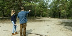 A man and a woman survey a wooded area of land.