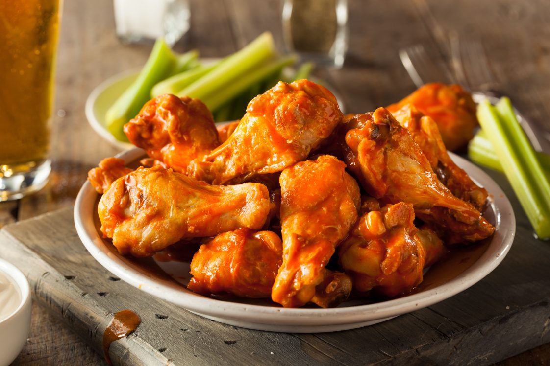 A plate of hot wings with celery and beer in the background.