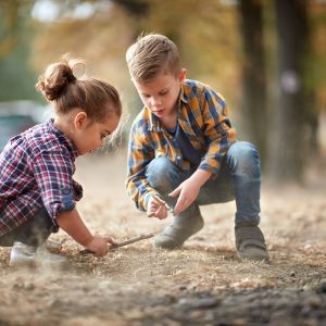 A young brother and sister playing with a stick on the ground.