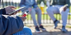 Close Up Of Teenagers With Mobile Phone Vaping and In Park