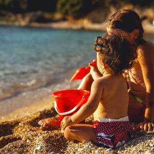 Two siblings sitting on a beach at near sunset, playing with a shovel and pale.