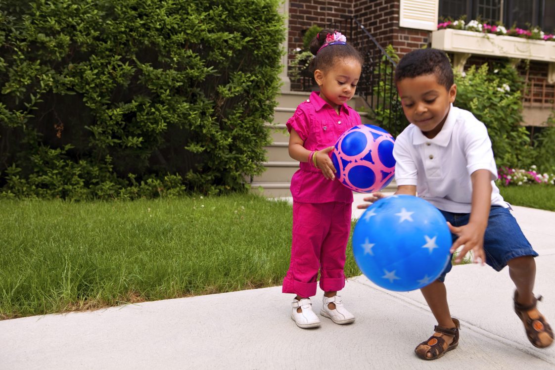 Young kids, seemingly a sister and brother, playing outside with a blue ball.