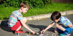 Two brothers having fun with picture drawing traffic car with chalks.