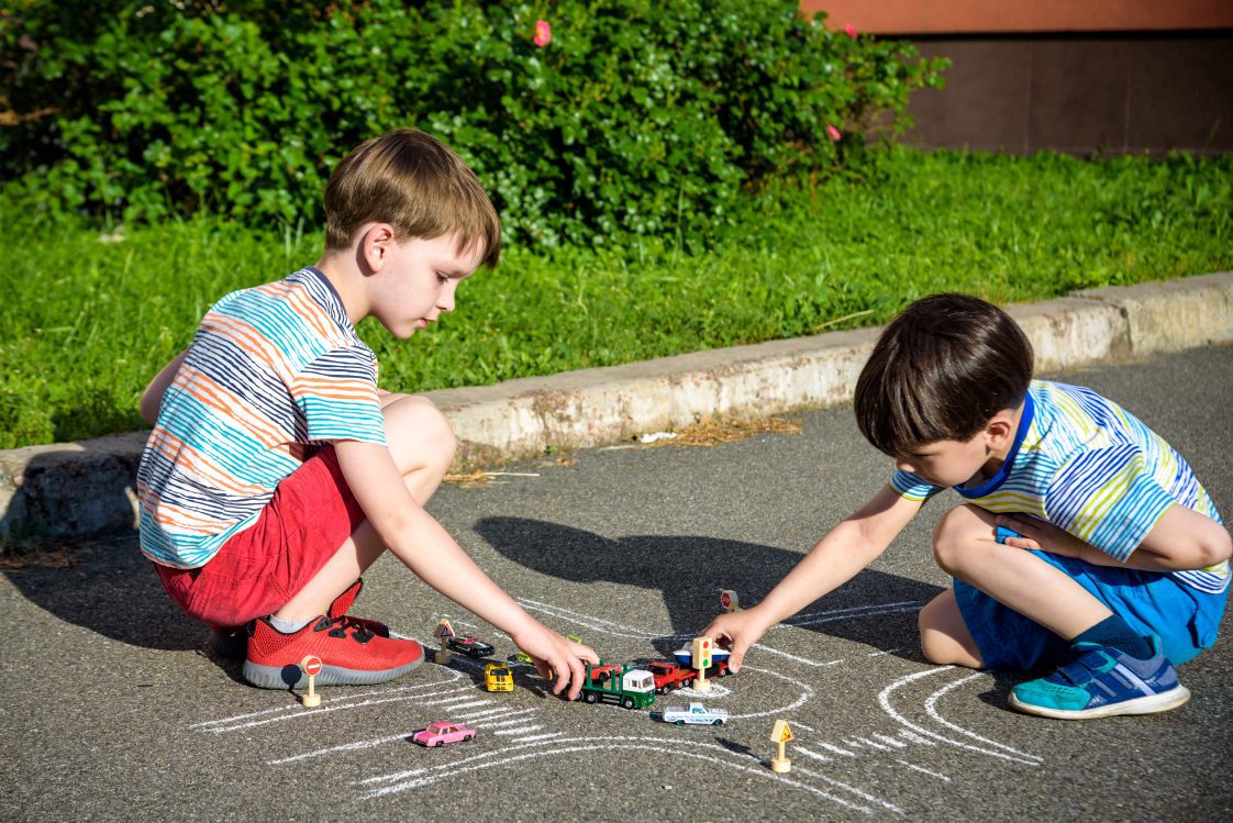 Two brothers having fun with picture drawing traffic car with chalks.