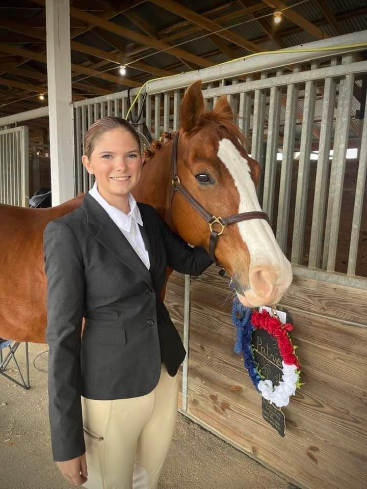 A 4-H member standing with her horse in a stable.