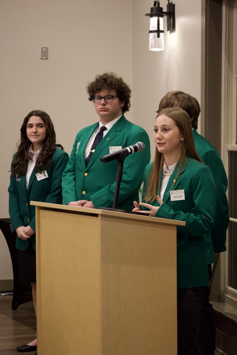 A 4-H Ambassador standing at a podium with others in the background. 