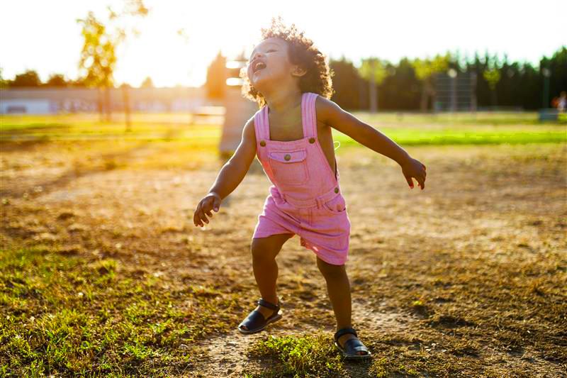 A young girl playing outside with the sun setting in the background.