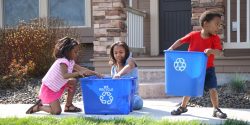 Three children putting items into recycle bins.