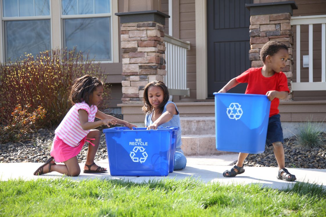 Three children putting items into recycle bins.