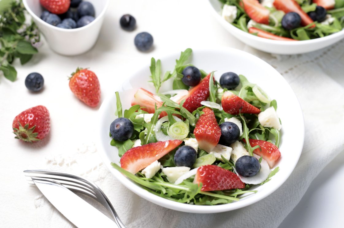 salad with strawberries, blueberries, arugula and feta cheese on white plate.