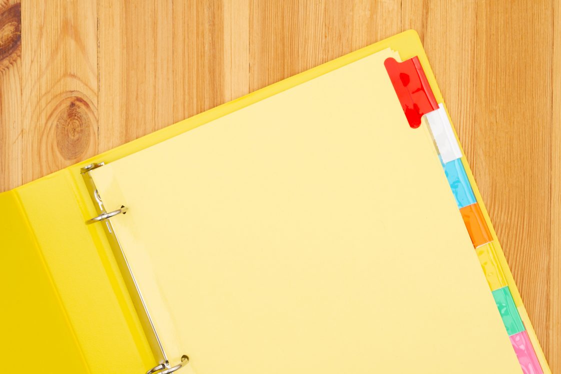 An opened, yellow school binder lying on a wooden table.