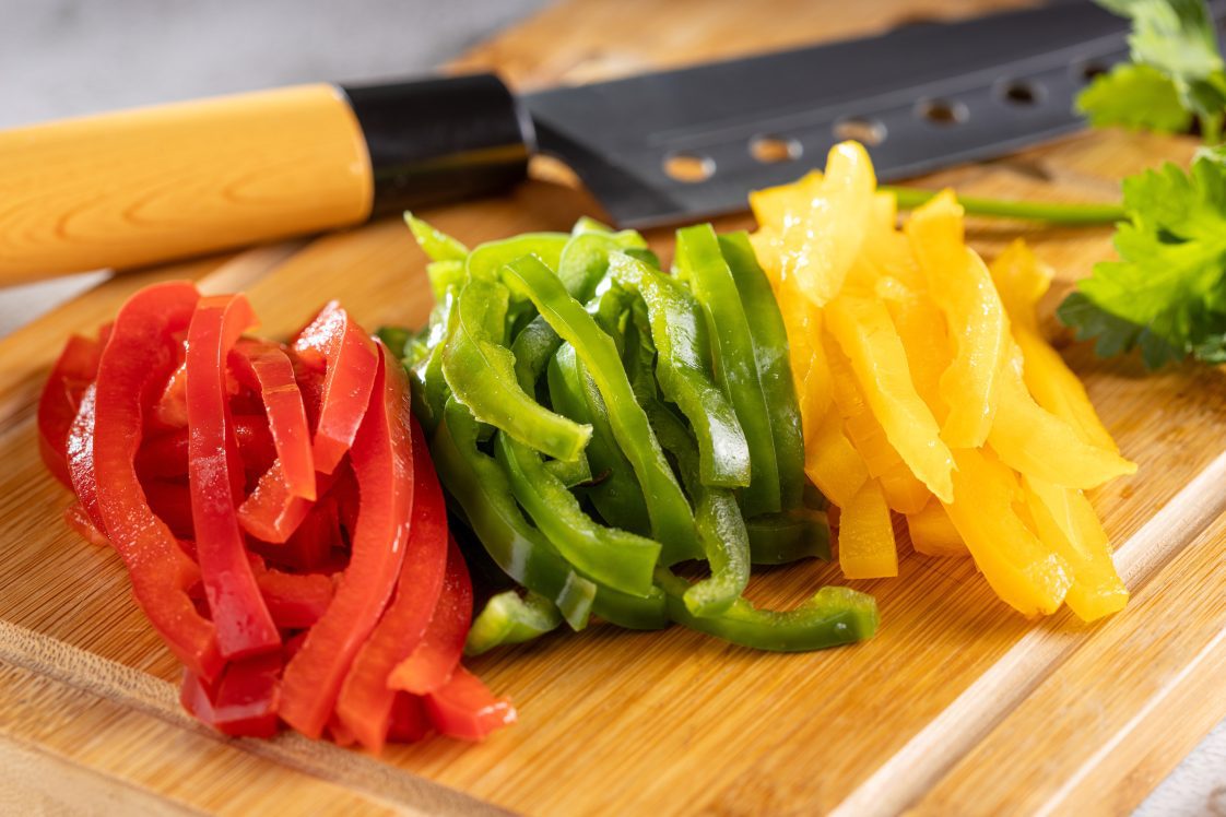 Sliced red, green, and yellow bell peppers on a cutting board.
