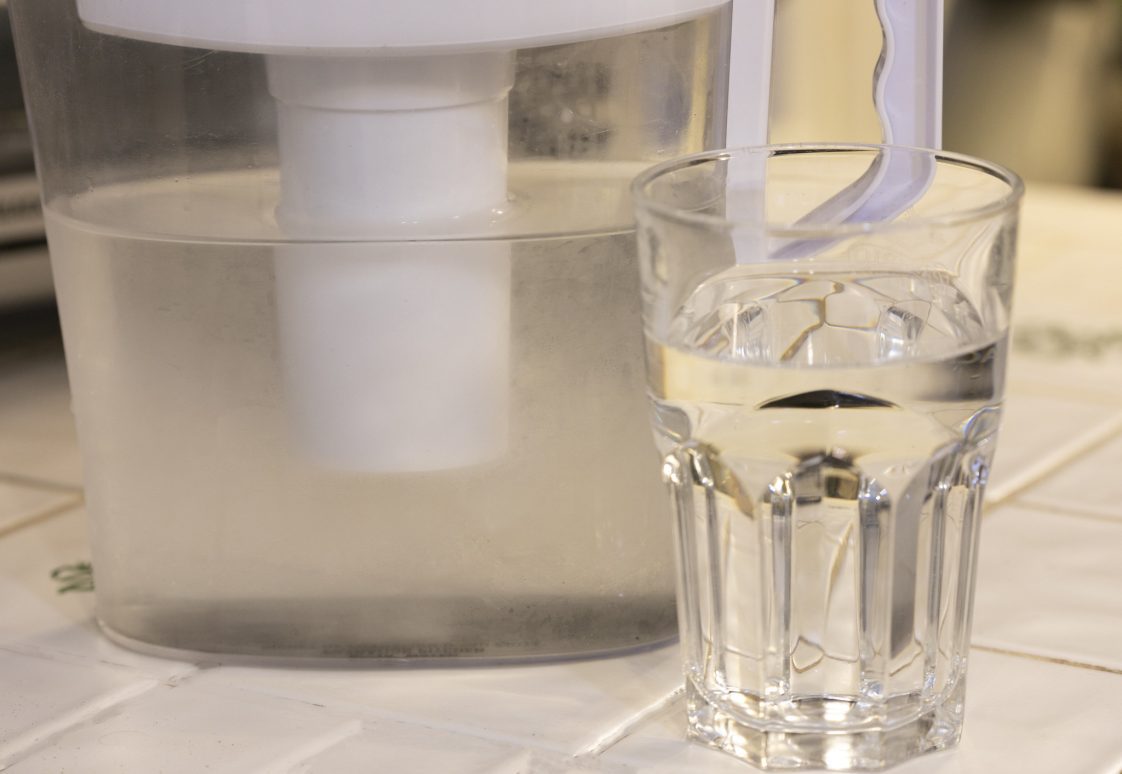 A glass and pitcher of water sitting on a kitchen counter.