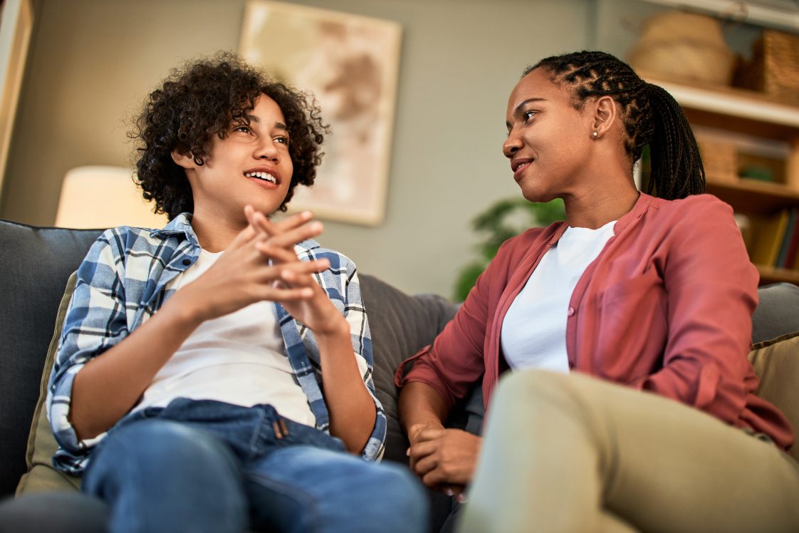 A teenage boy talking to his mother while sitting on a couch.