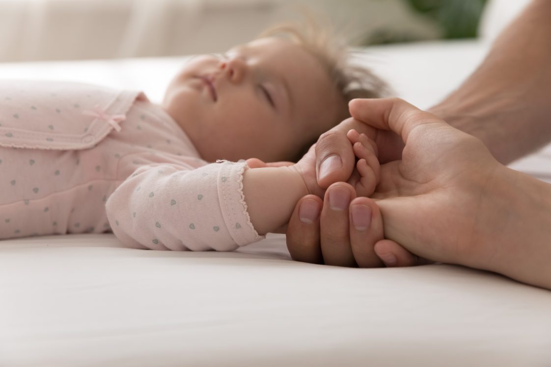baby sleeping on their back and holding an adult hand
