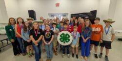 A large group of 4-H'ers standing in a room with one holding a 4-H sign.