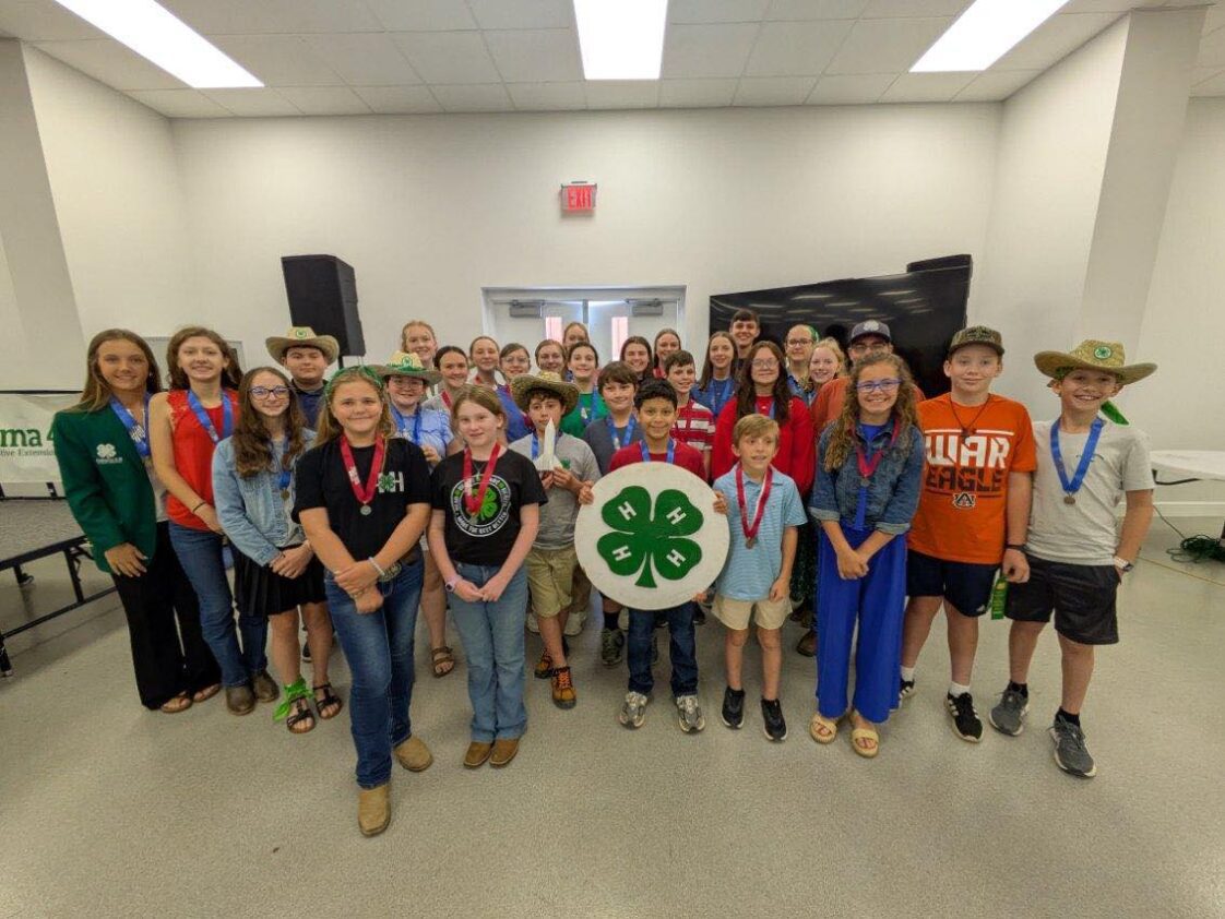 A large group of 4-H'ers standing in a room with one holding a 4-H sign.