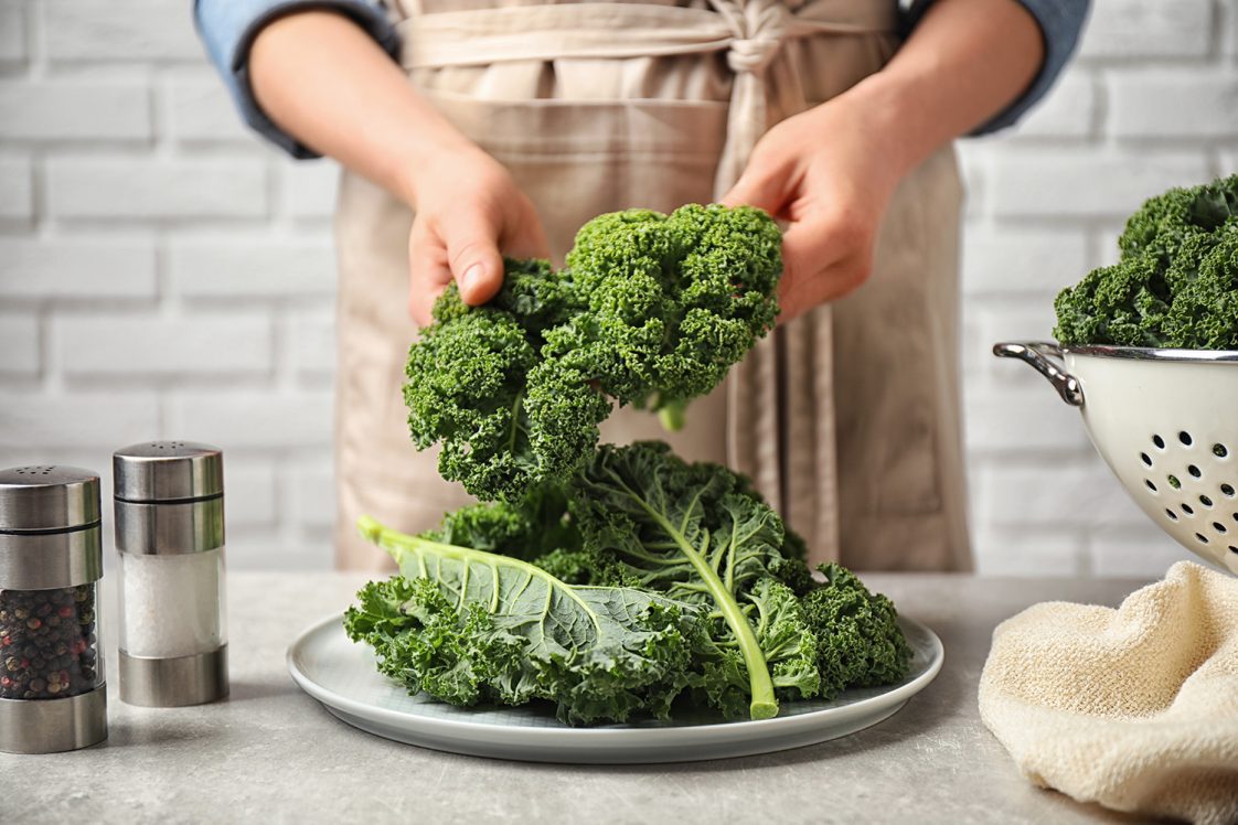 Woman holding fresh kale leaves over light grey table