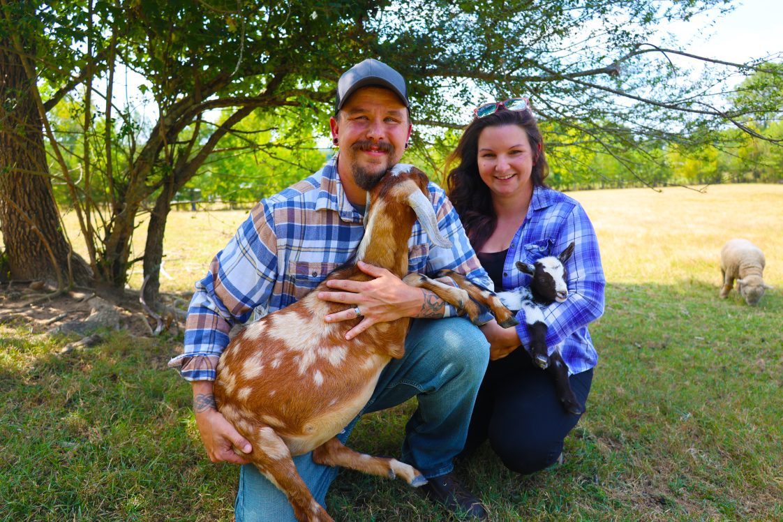 A man and woman each holding a goat in their arms.