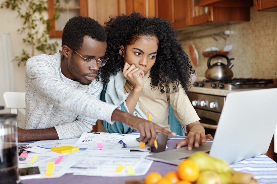 A husband and wife looking at a laptop and surrounded by financial papers.