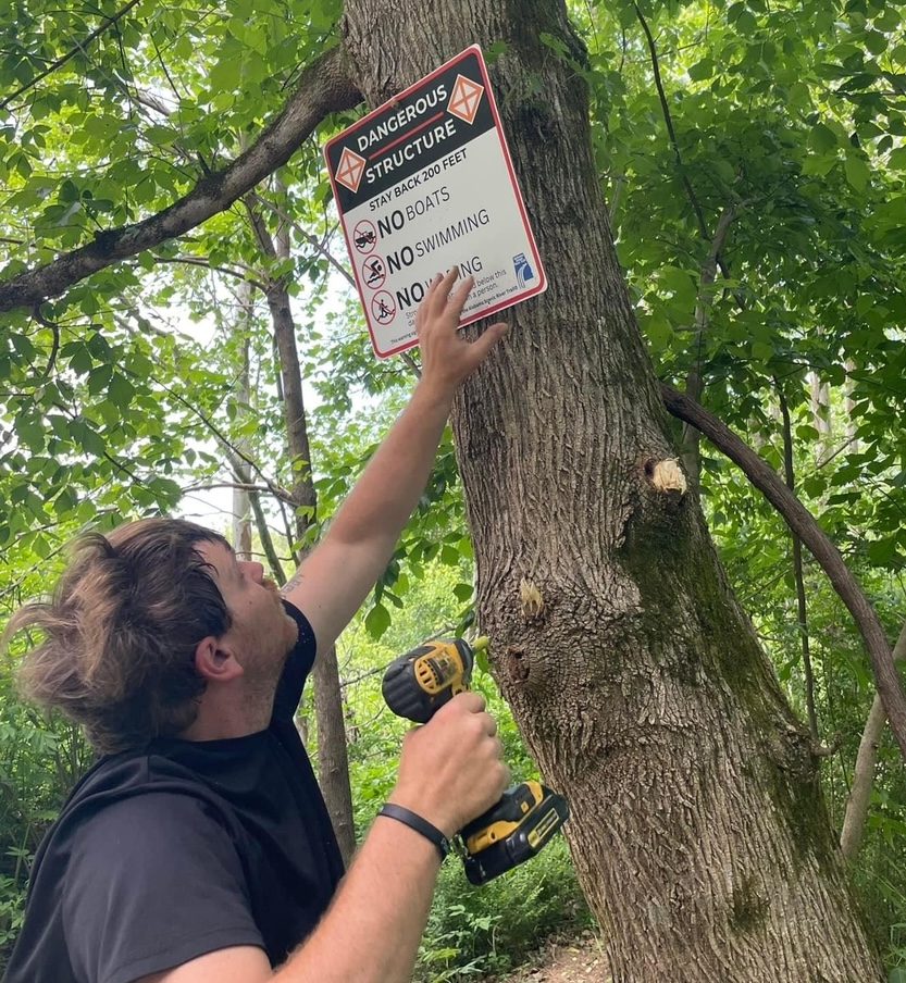 A man installing a sign upstream of a low-head dam.