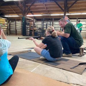 Tim Gothard demonstrates proper seated rifle form, working with 4-H members at a Shooting Sports event.