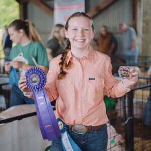 A 4-H member holding a purple ribbon for Supreme Showman at the Limestone County Pig Squeal.