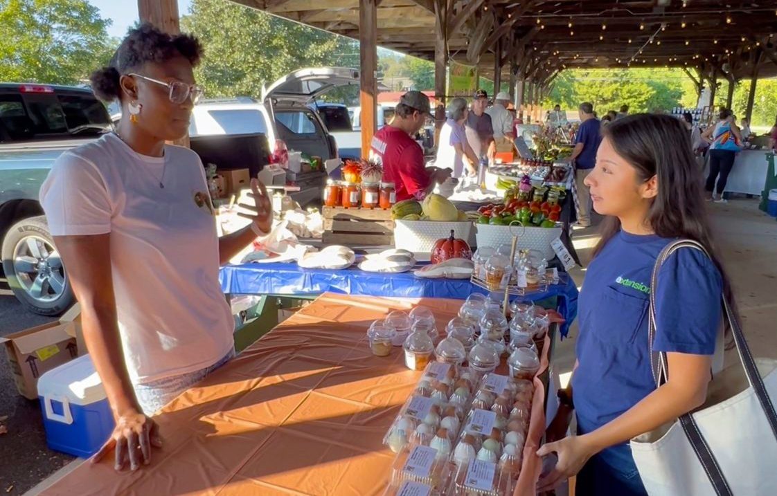 A member of the Chaidez family talking with Extension Agent Roshell Rosales Aguilar at a farmers market.