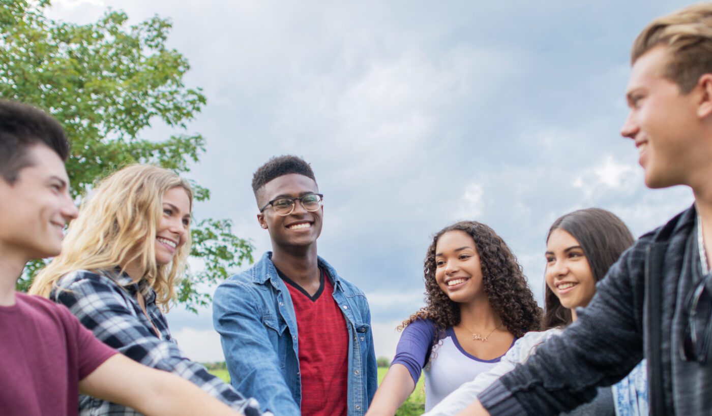 A small group of teens stand in a circle with their hands stacked in the middle 