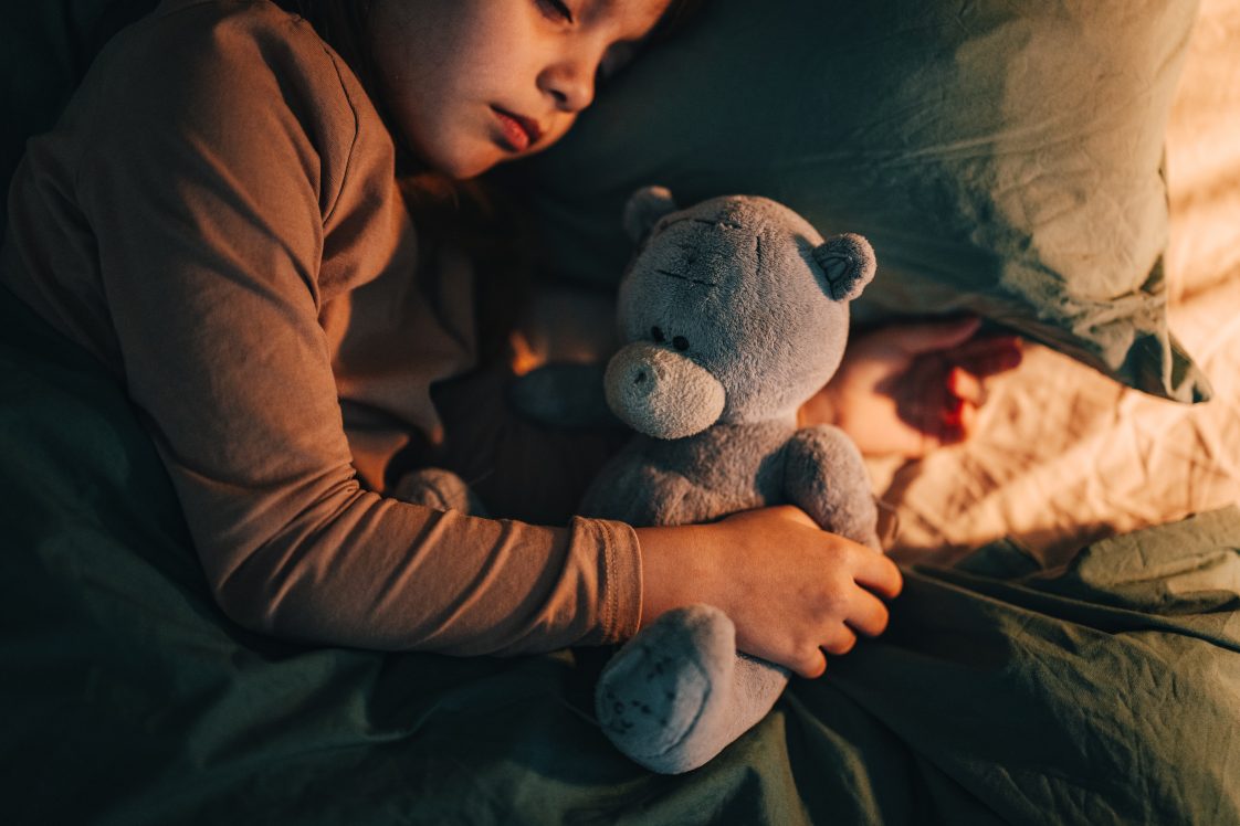 High angle view of an anonymous girl embracing her toy while lying in the bed at home.