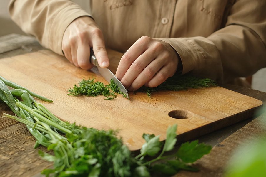 Female hands chopping fresh dill on wooden cutting board