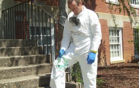 A person wearing pesticide applicator safety gear looking tired and hot after working outside.