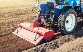 A blue tractor pulling a red tiller in a garden.