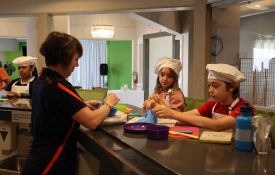 An educator hands out plastic gloves to 4M Youth Camp participants as they prepare a recipe.