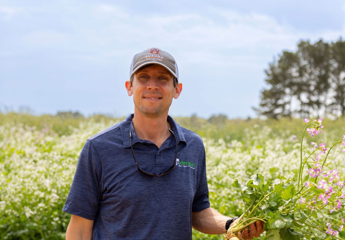 David-Russell standing on the edge of a field holding a purple and green plant.