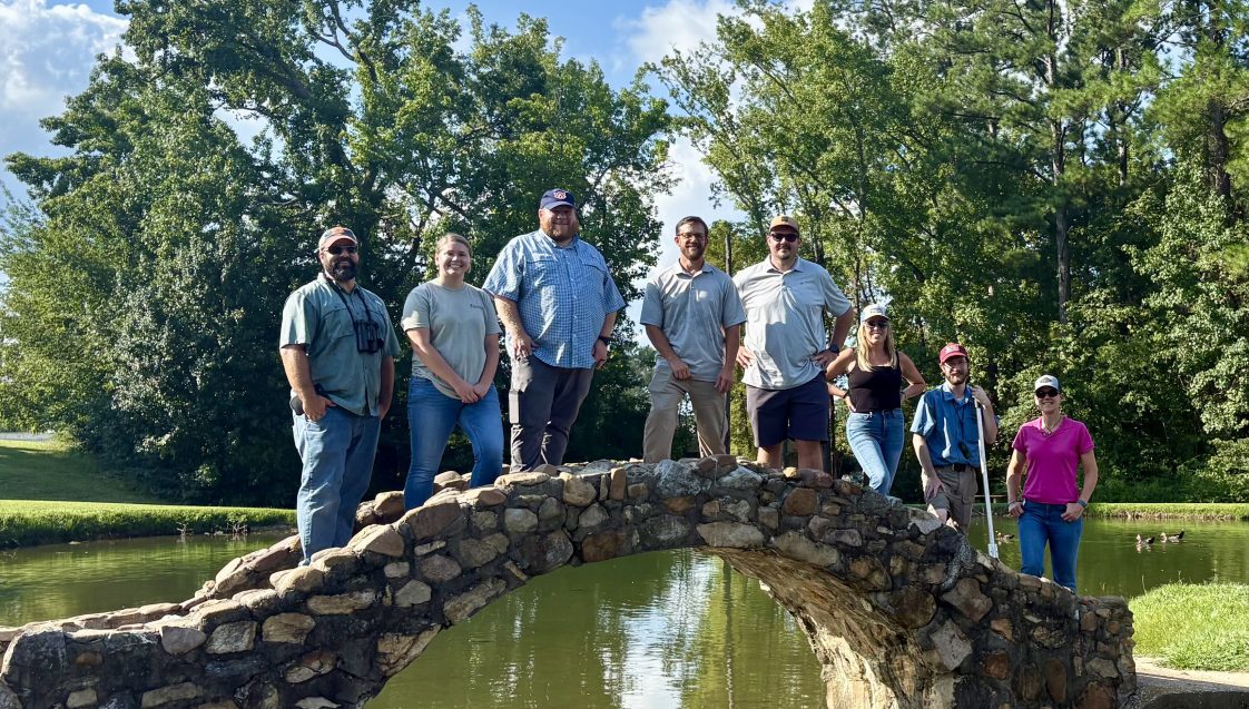 Alabama Extension professionals posing for a picture on a rock bridge over a pond.