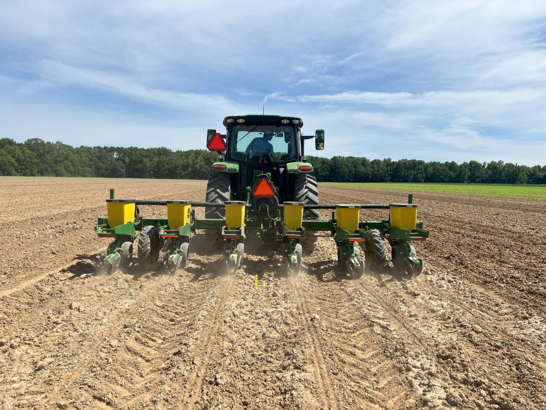 A farmer driving a tractor with attached planted down a fallow field.