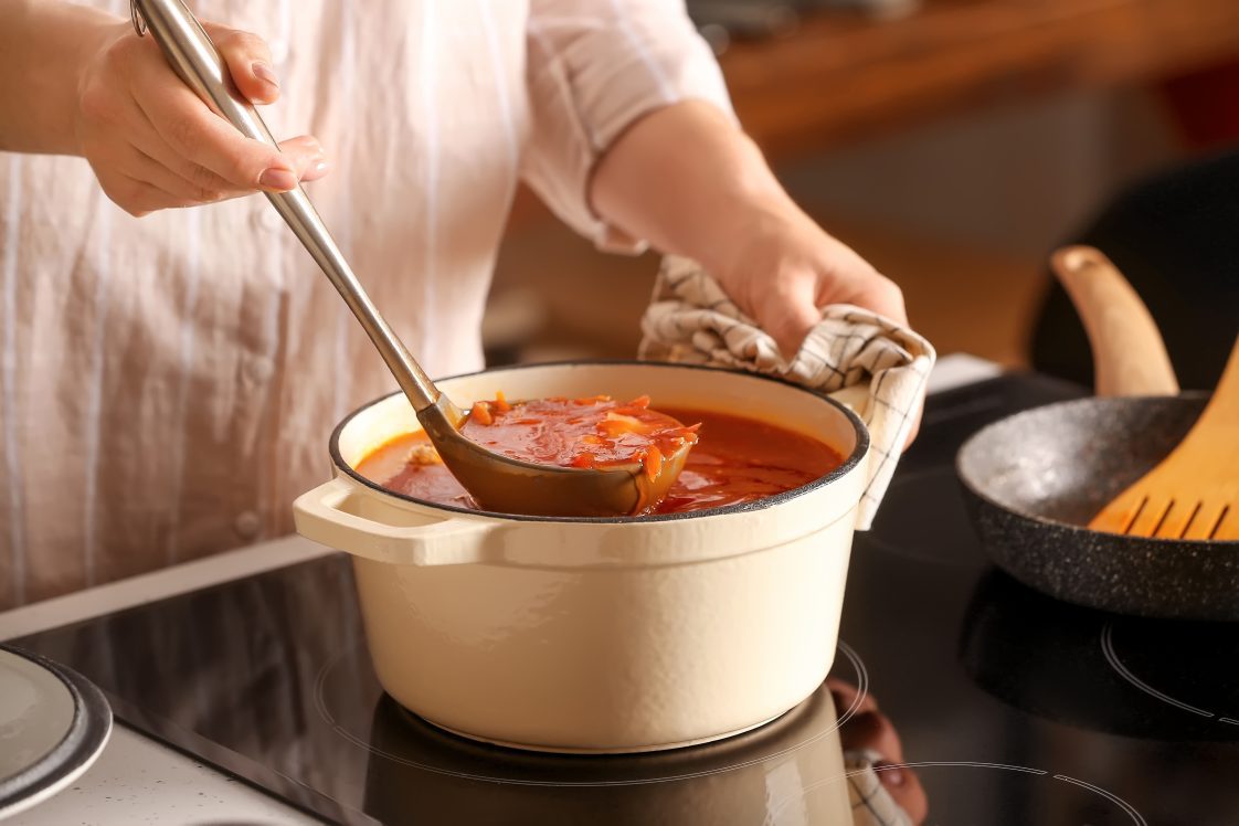 A woman ladling soup out of a pot on the stove top.