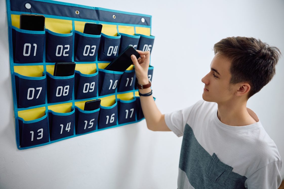 Student putting smartphone in wall hanging in a classroom.