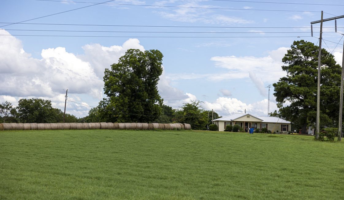 A small farm house next to a hay field.