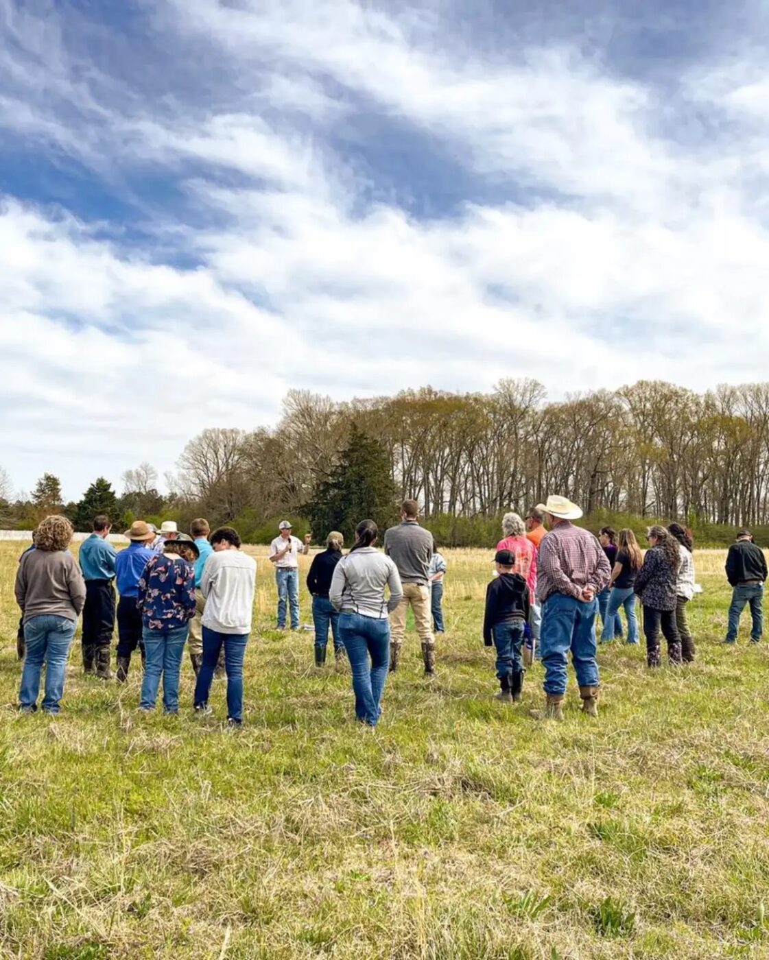 A group of people in a pasture listening to a speaker talk about weed management.