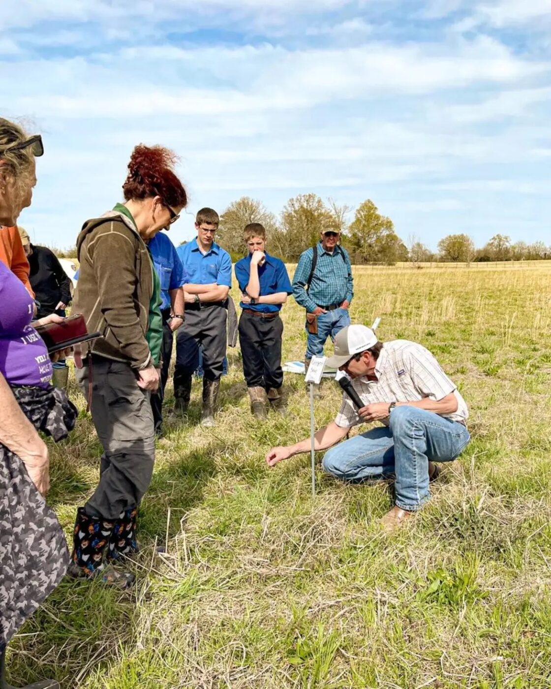 Extension specialist talking to a group of people about weed management in a pasture.