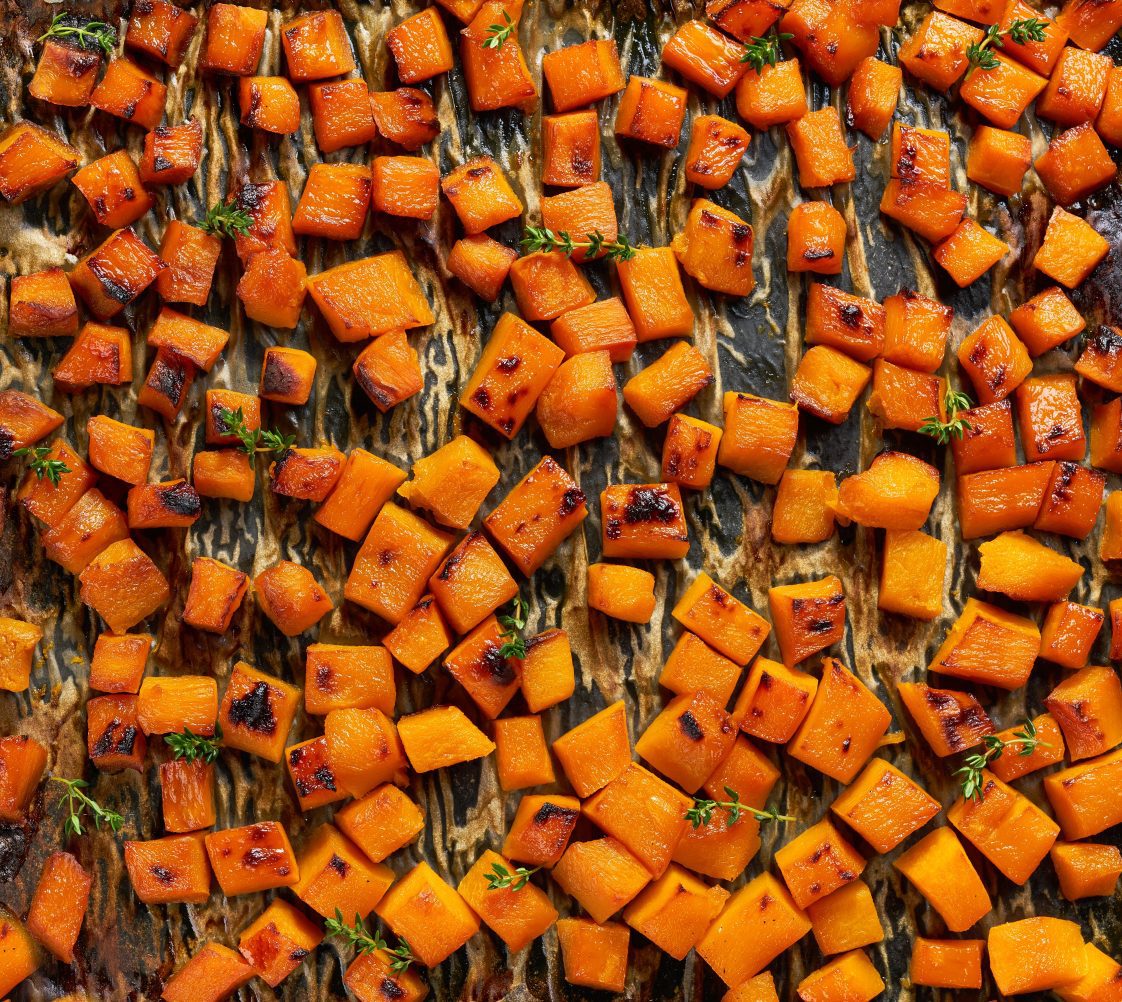 Cubes of roasted butternut squash and herbs on a sheet pan lined with parchment.