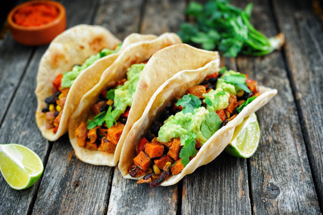 Three black bean tacos and the trimmings sitting on wood-grain surface.