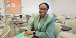 A photo of Portia Johnson in a classroom. She is wearing a light green suit while sitting in a desk.