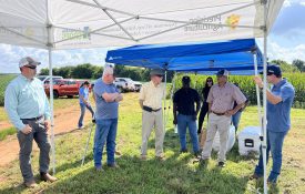 A group of people standing underneath a tent outside at a crop field day.