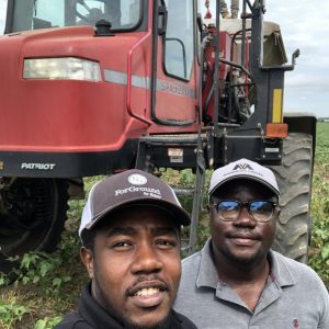 Two men posed for selfie picture in front of farm equipment in a field.