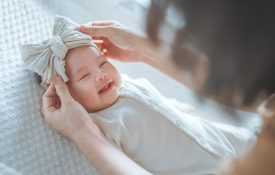 A closeup of a happy, smiling baby wearing a bow while lying on a bed.