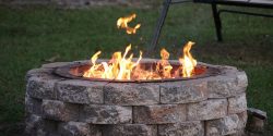 A stone fire pit with a light fire in a backyard.